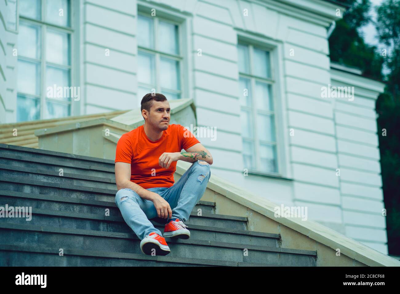Un jeune homme dans un t-shirt rouge et un Jean pose sur les escaliers du domaine. Un homme adulte en baskets rouges est assis sur les marches du Palais. Banque D'Images