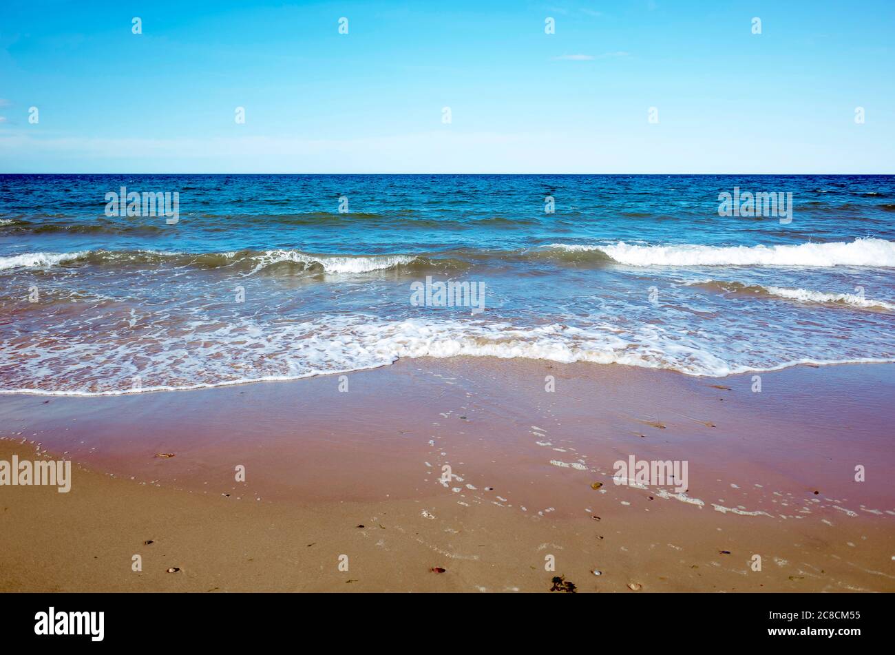 Mer calme petites vagues se brisant sur une plage de sable ciel clair horizon net Banque D'Images