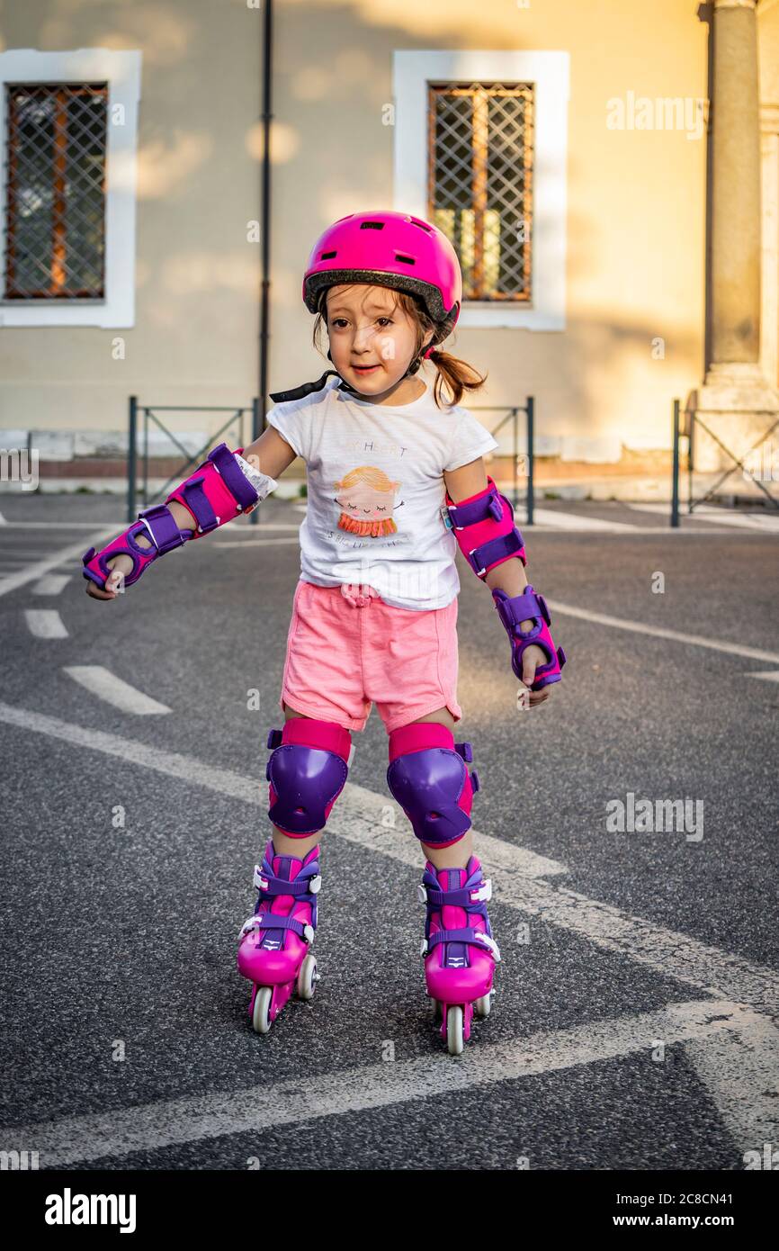 Une petite fille (enfant) apprend à roller dans la rue dans la ville.  Sécurité avec casque et protections pour les coudes, les poignets et les  genoux. Concepts : plaisir, s Photo Stock -