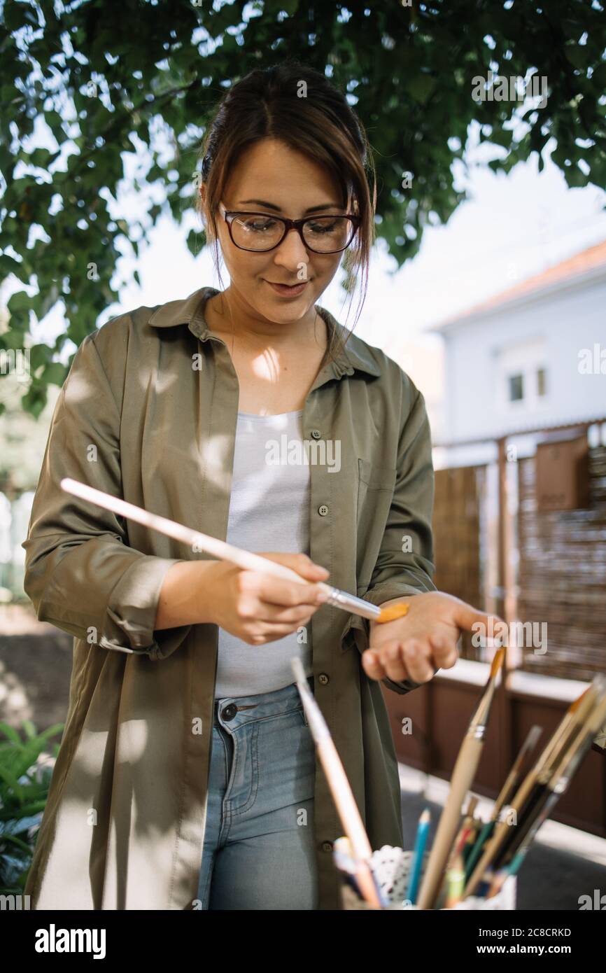 Portrait d'une artiste féminine frottant une nouvelle brosse de peinture sur sa main Banque D'Images