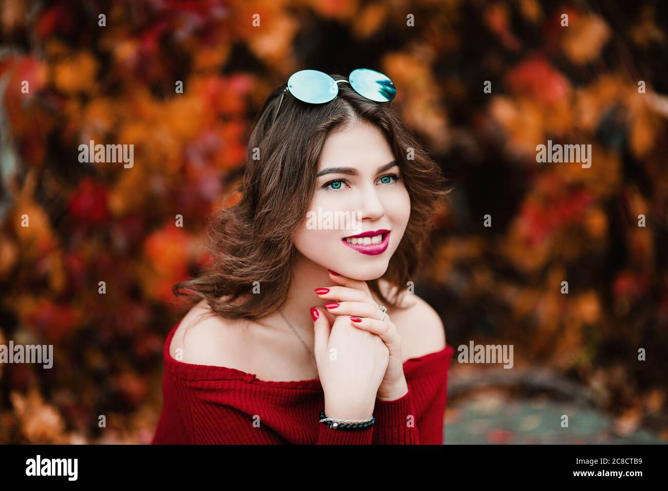 Belle jeune femme décontractée en lunettes assis parmi les feuilles jaunes et rouges dans le parc public, couleurs d'automne fond Banque D'Images