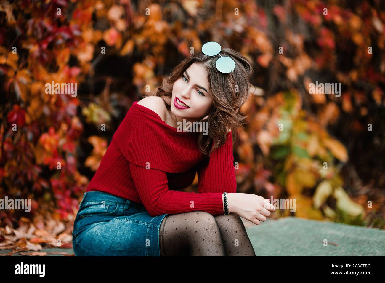 Belle jeune femme décontractée en lunettes assis parmi les feuilles jaunes et rouges dans le parc public, couleurs d'automne fond Banque D'Images