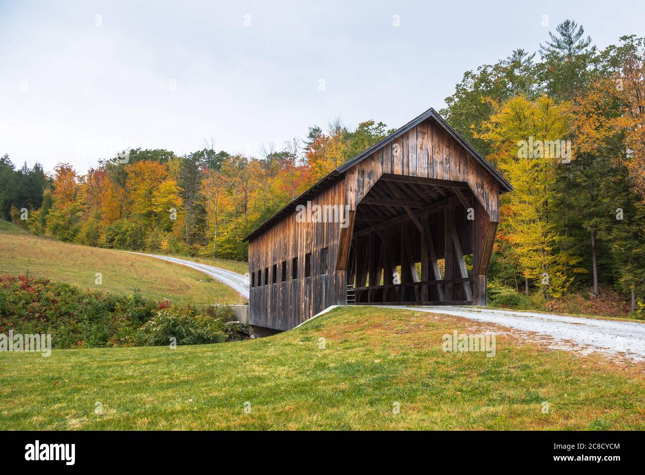 Vieux pont couvert le long d'une route de gravier dans le Vermont lors d'une journée d'automne nuageux Banque D'Images
