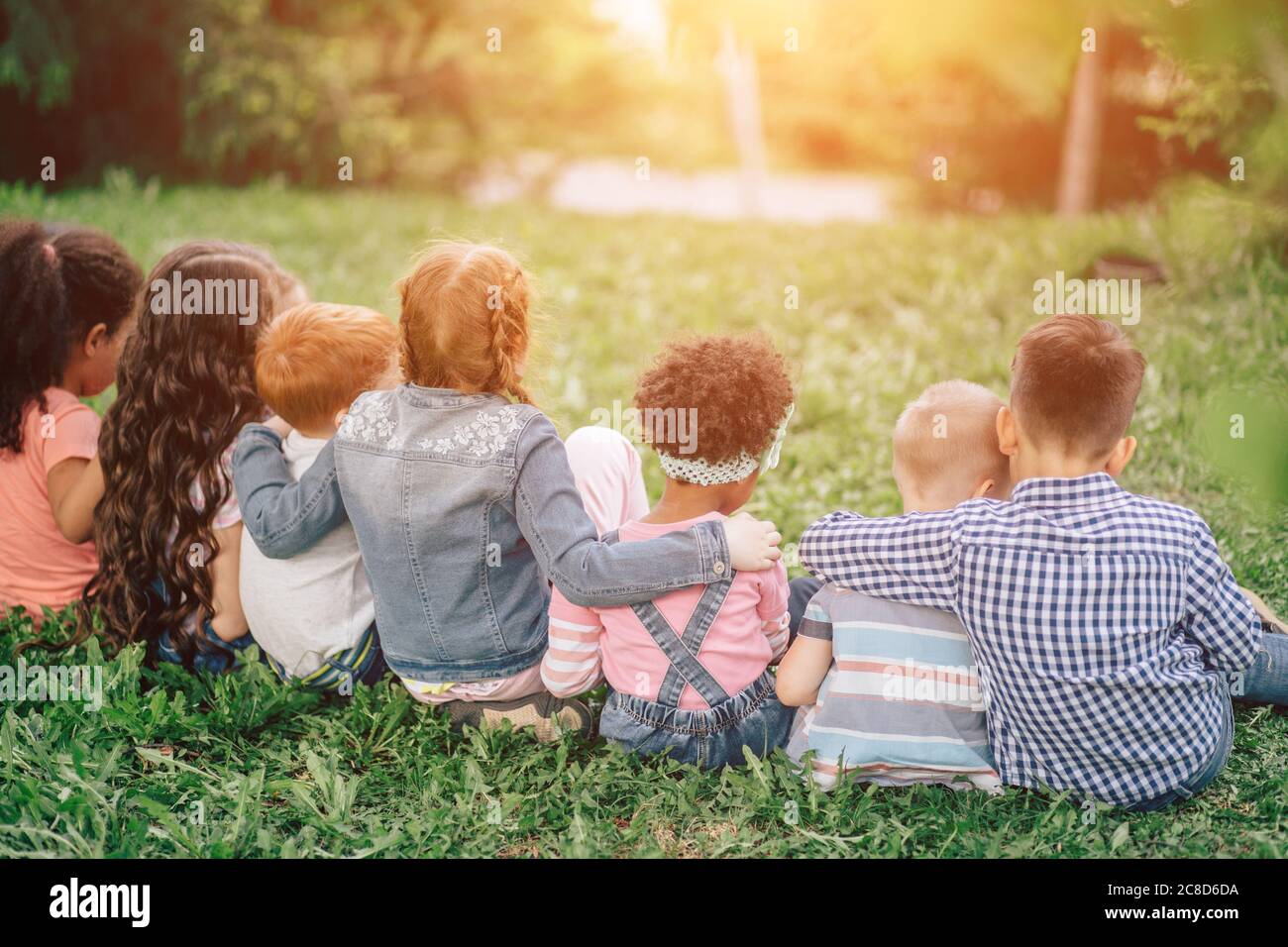 Vue arrière de jolis enfants assis sur l'herbe verte et de détente. Extérieur. Le concept de l'enfance et de l'amitié. Banque D'Images