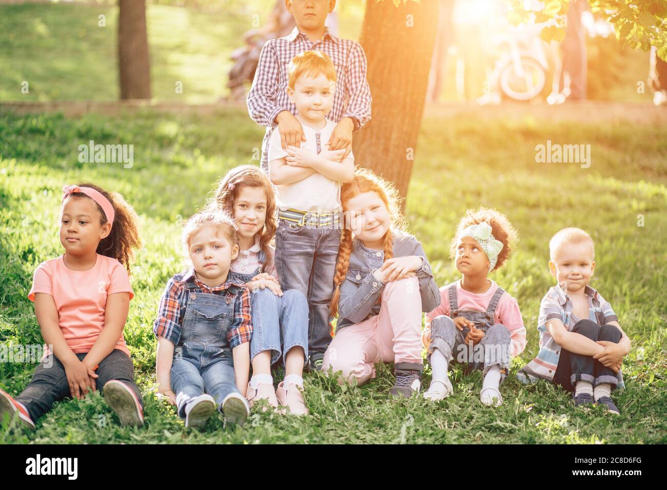 Petits garçons et filles assis sur l'herbe et embrassant. Dans le parc. Le concept de l'enfance, de l'amitié et de la communication multiculturelle. Banque D'Images