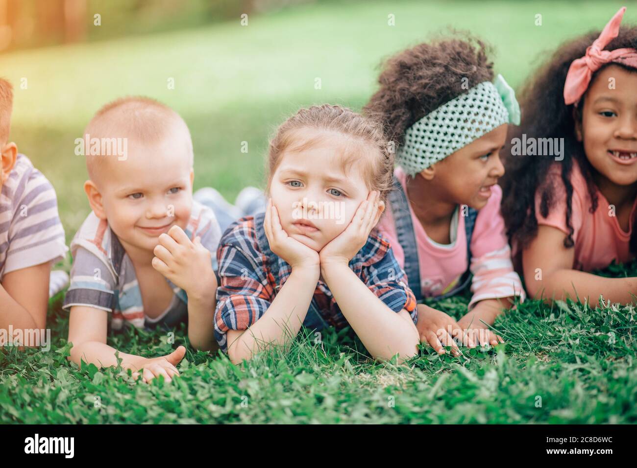 Belle fille couchée sur l'herbe avec ses amis. Le concept de l'enfance, de l'amitié et de la communication interculturelle. Banque D'Images