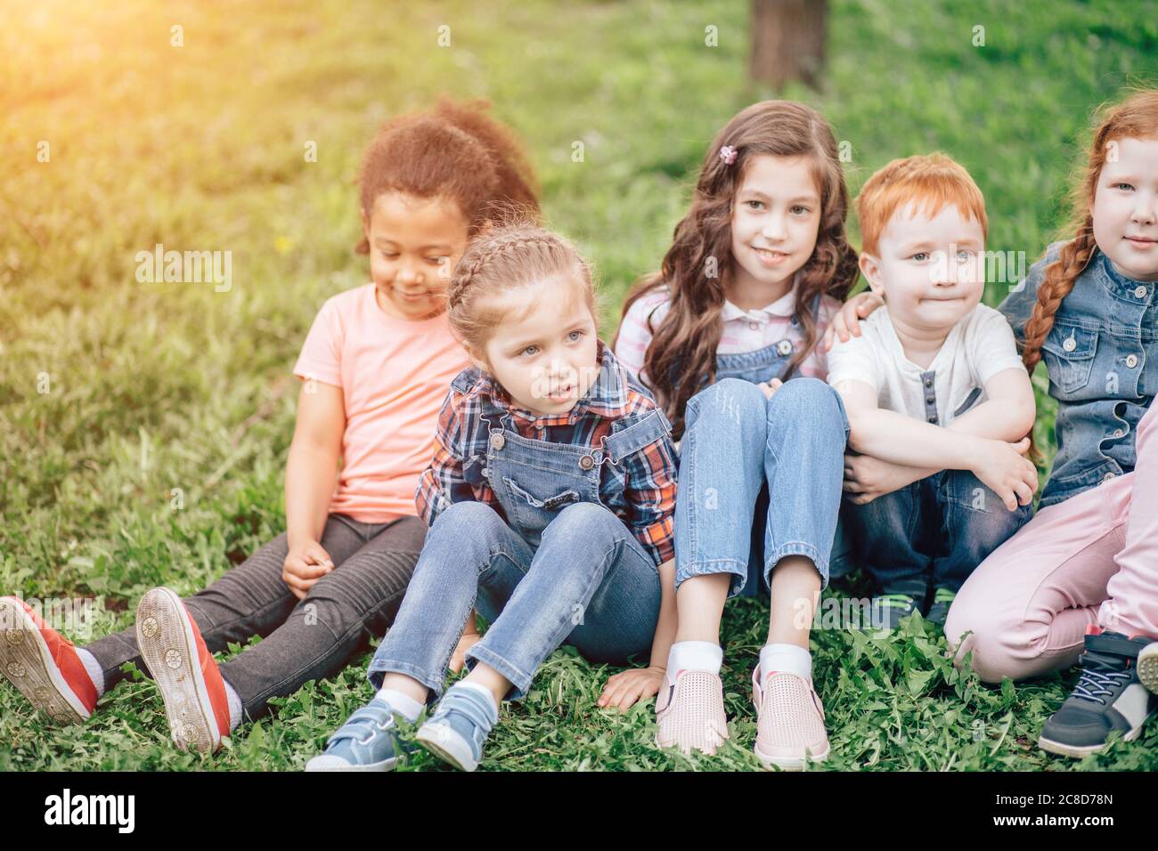 Image de garçons et filles heureux assis sur l'herbe verte. Le concept de l'enfance, de l'amitié et de la communication multiculturelle Banque D'Images