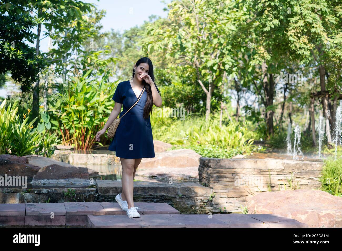 Bonne femme à cheveux longs dans la robe bleu foncé riggle en marchant sur l'escalier en pierre dans le parc pendant sa datation. Banque D'Images