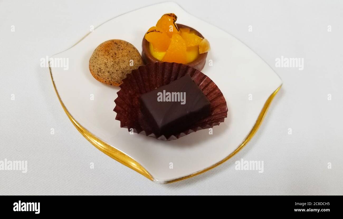 une assiette en porcelaine décorative à bords dorés. Sur elle, il y a une tarte aux fruits de la taille d'une bouchée, une boule de gâteau et un morceau de chocolat servi Banque D'Images