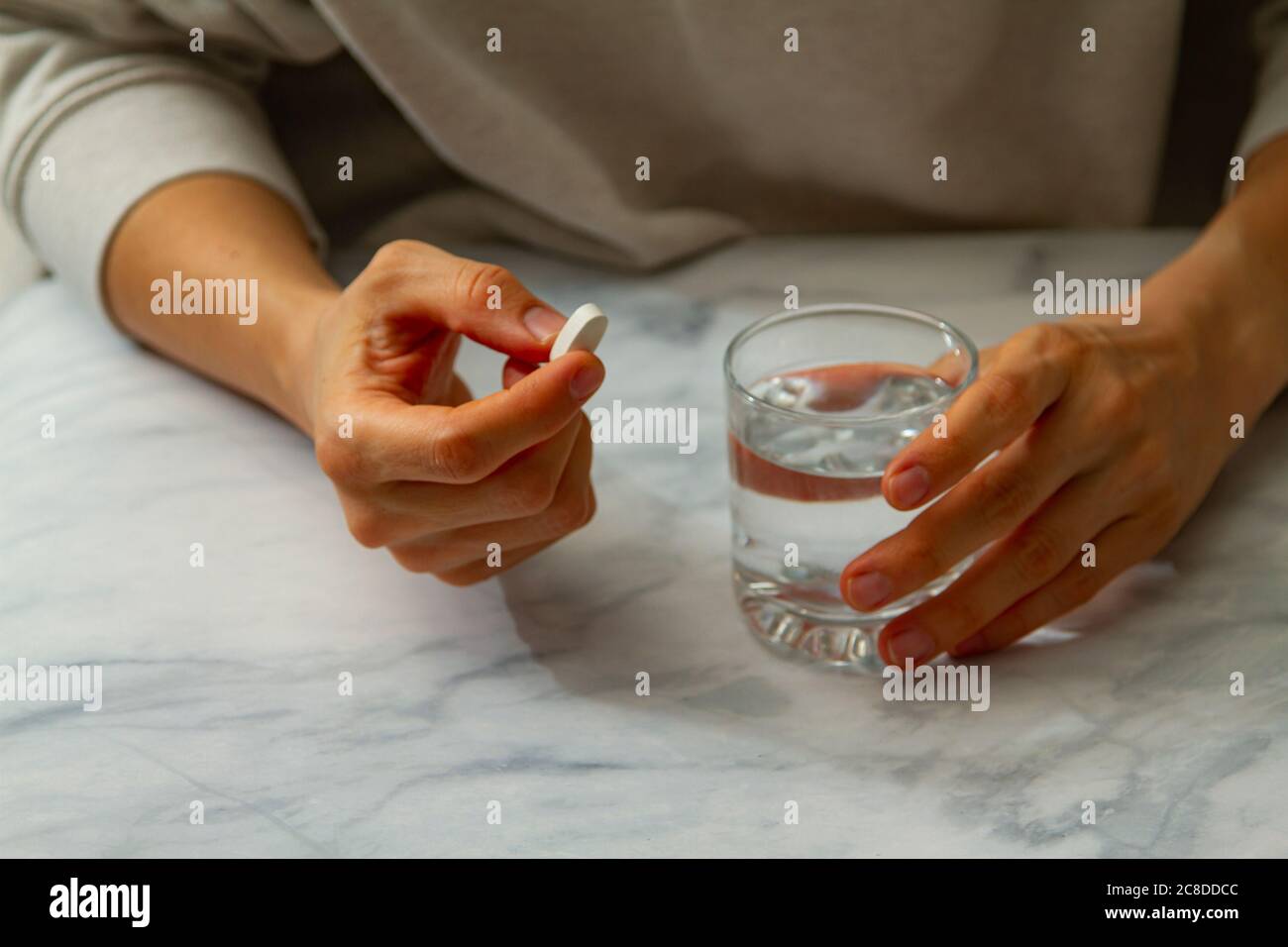Une femme est vue comme elle tient une pilule dans une main et un verre d'eau de l'autre main. Elle est sur le point de prendre le médicament avec une gorgée d'eau. Banque D'Images