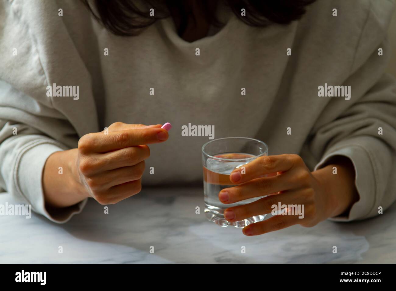 Une femme est vue comme elle tient une pilule dans une main et un verre d'eau de l'autre main. Elle est sur le point de prendre le médicament avec une gorgée d'eau. Banque D'Images
