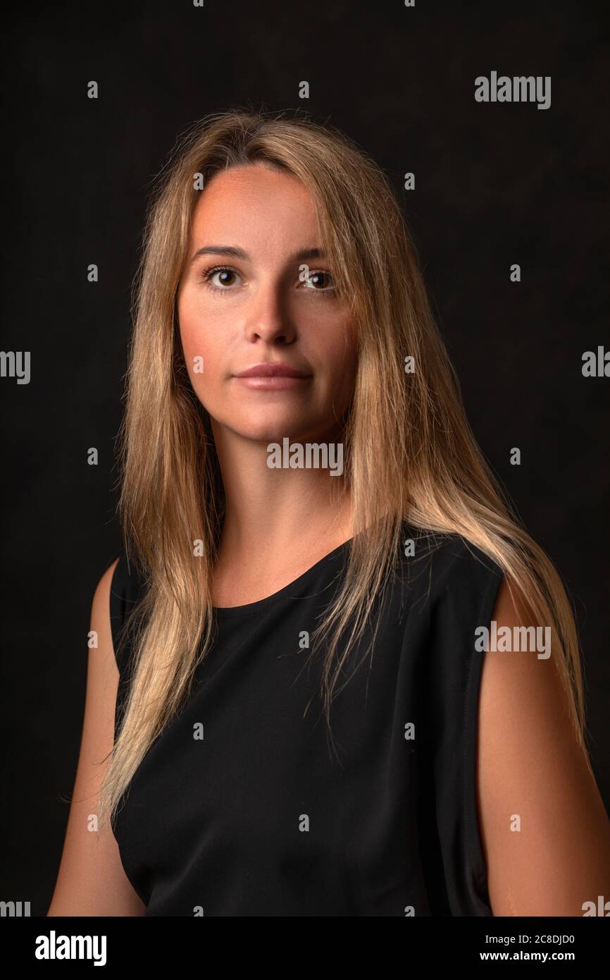 Calme paisible belle fille dans une robe noire sur un fond sombre, portrait d'une femme de 30 ans avec de longs cheveux blonds. Prise de vue en studio verticale triste. Banque D'Images