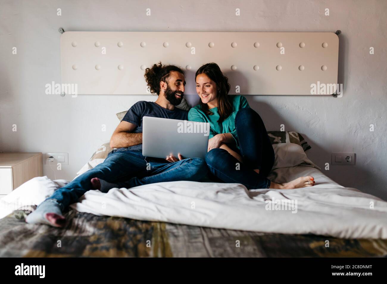 Couple regardant un film assis sur le lit à la maison Banque D'Images