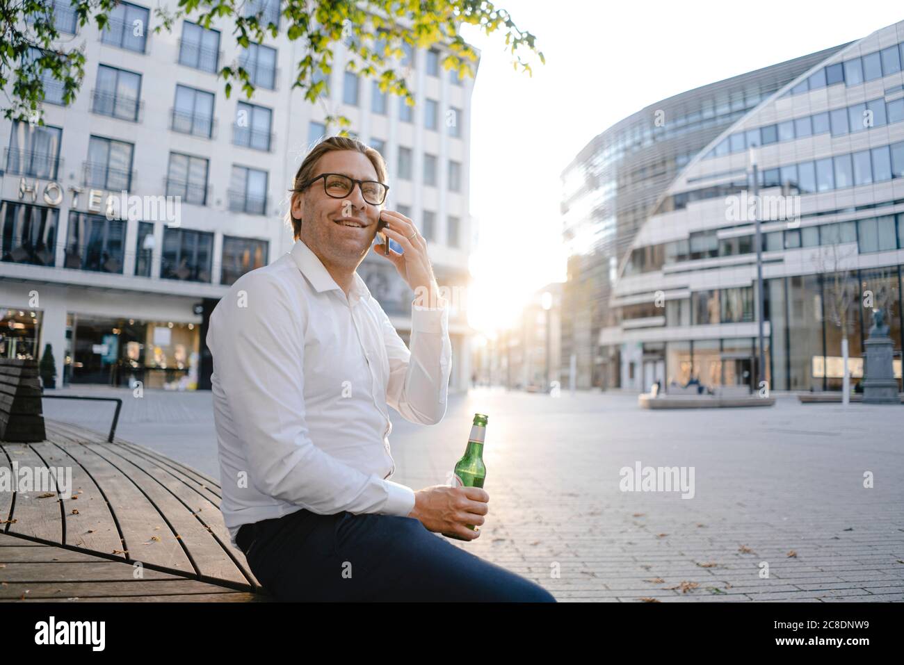 Homme d'affaires assis sur un banc dans la ville au coucher du soleil parler au téléphone Banque D'Images