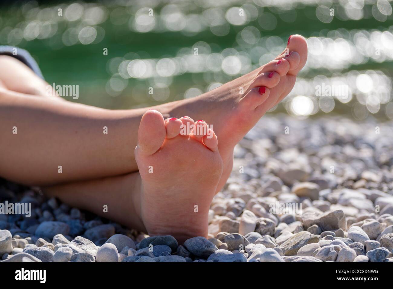 Jeune femme pieds nus assise sur des galets au bord de la rivière Banque D'Images