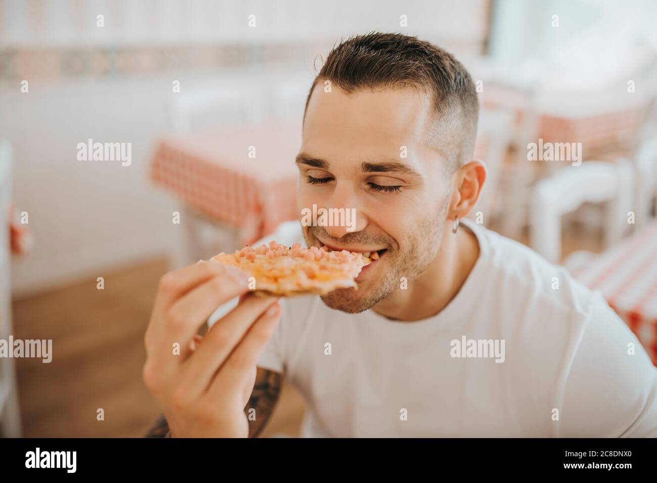 Gros plan du jeune homme avec les yeux fermés manger de la pizza pendant assis dans le restaurant Banque D'Images