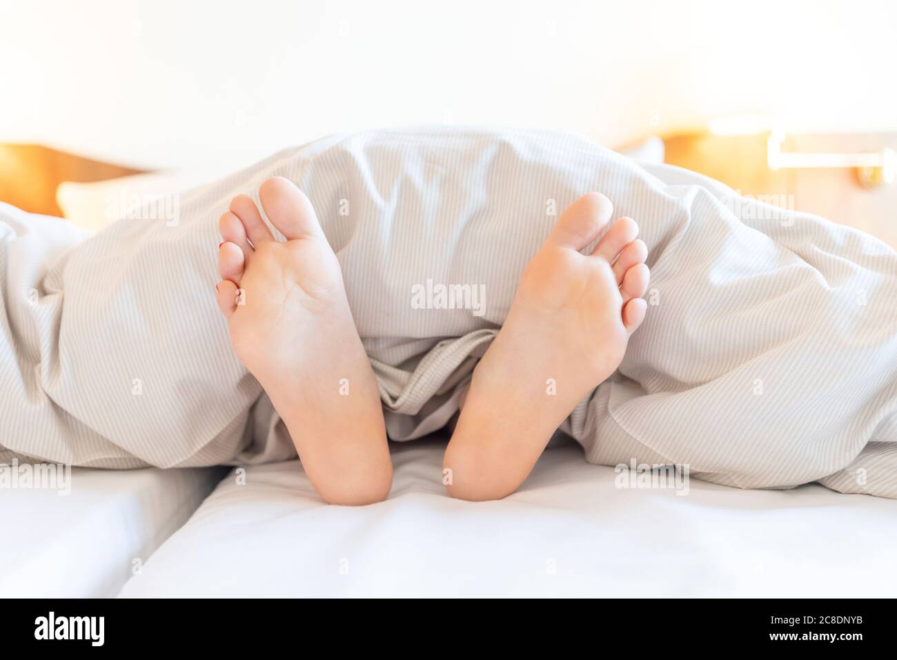 Gros plan d'une femme pieds nus se détendant au lit à la maison Banque D'Images