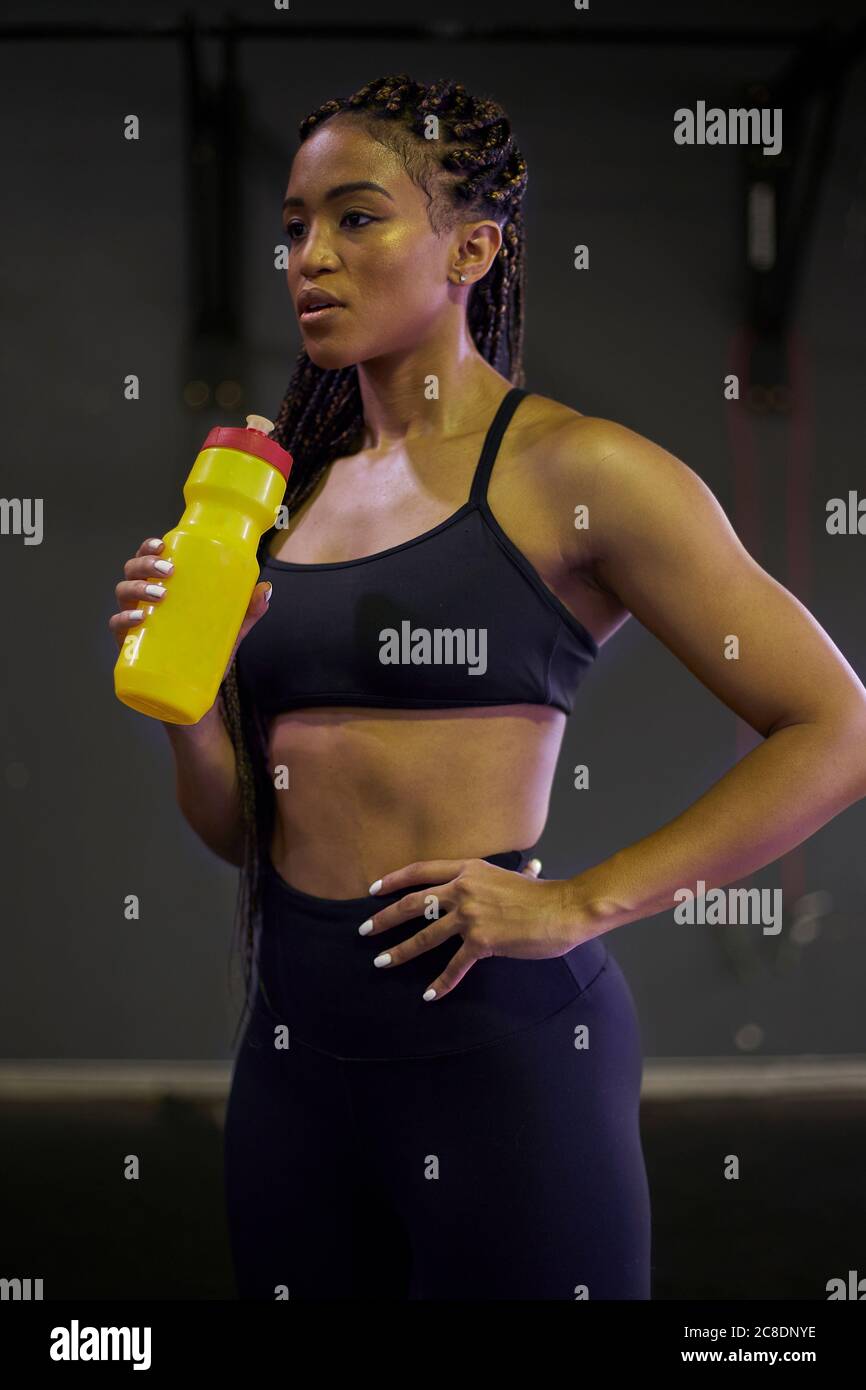 Une athlète féminine attentionnée tenant une bouteille d'eau tout en se tenant à la salle de gym Banque D'Images