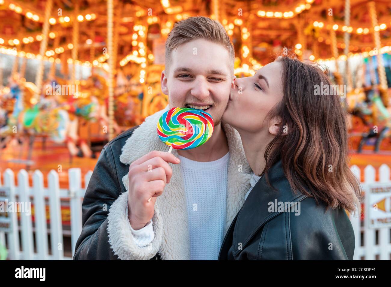 Gros plan de la femme embrassant sur le petit ami cheek mangeant la lollipop à parc d'attractions Banque D'Images