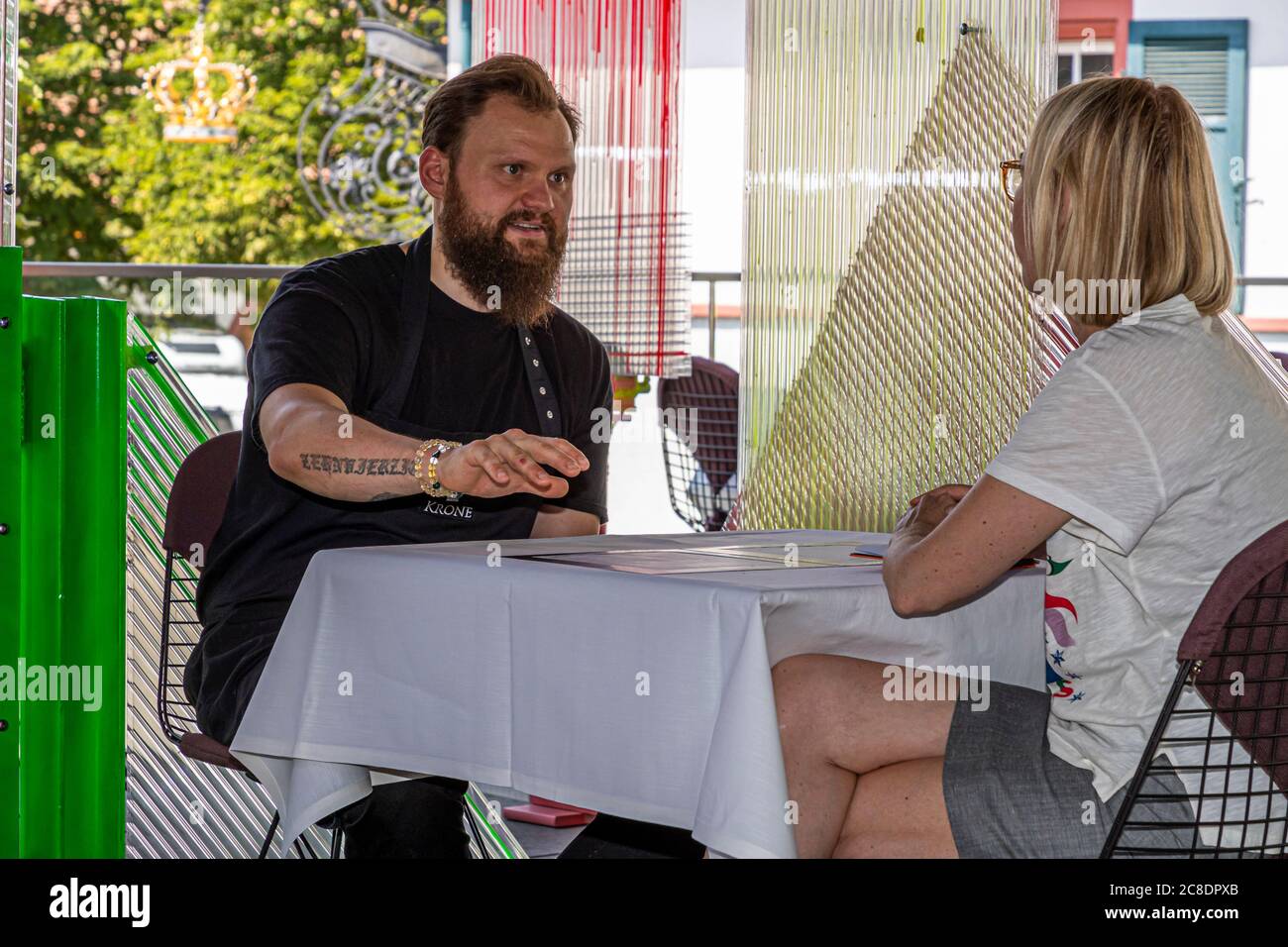 Restauration extérieure avec cloisons artistiquement conçues et serveurs avec masques de protection à l'Hôtel Krone à Weil am Rhein, Allemagne. Le chef Peter Prüfer en conversation avec la journaliste alimentaire Angela Berg Banque D'Images