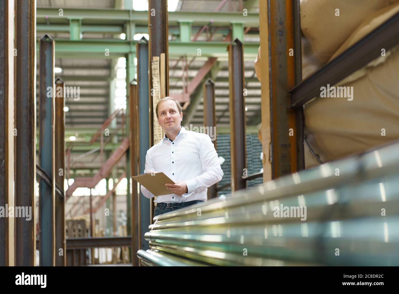 Homme d'affaires avec presse-papiers dans des tuyaux en acier dans une usine Banque D'Images