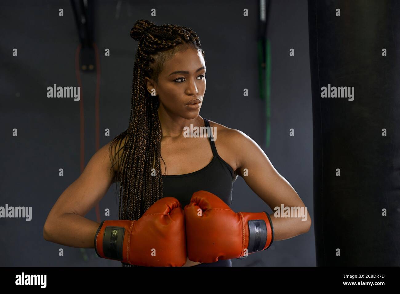 Jeune femme aux cheveux tressés portant des gants de boxe rouges salle de sport Banque D'Images