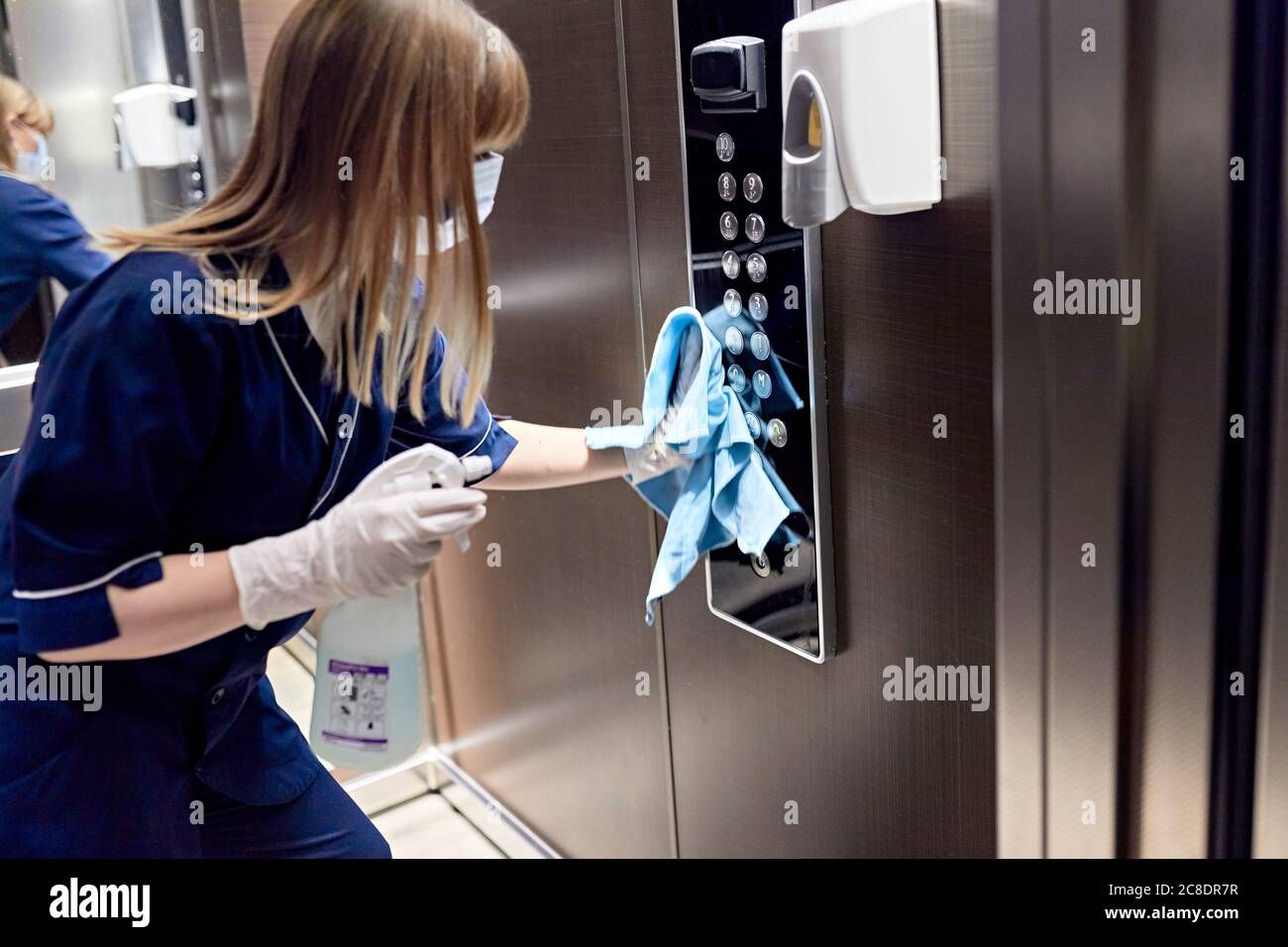 Femme de chambre portant un masque de nettoyage des boutons de l'ascenseur à l'hôtel Banque D'Images