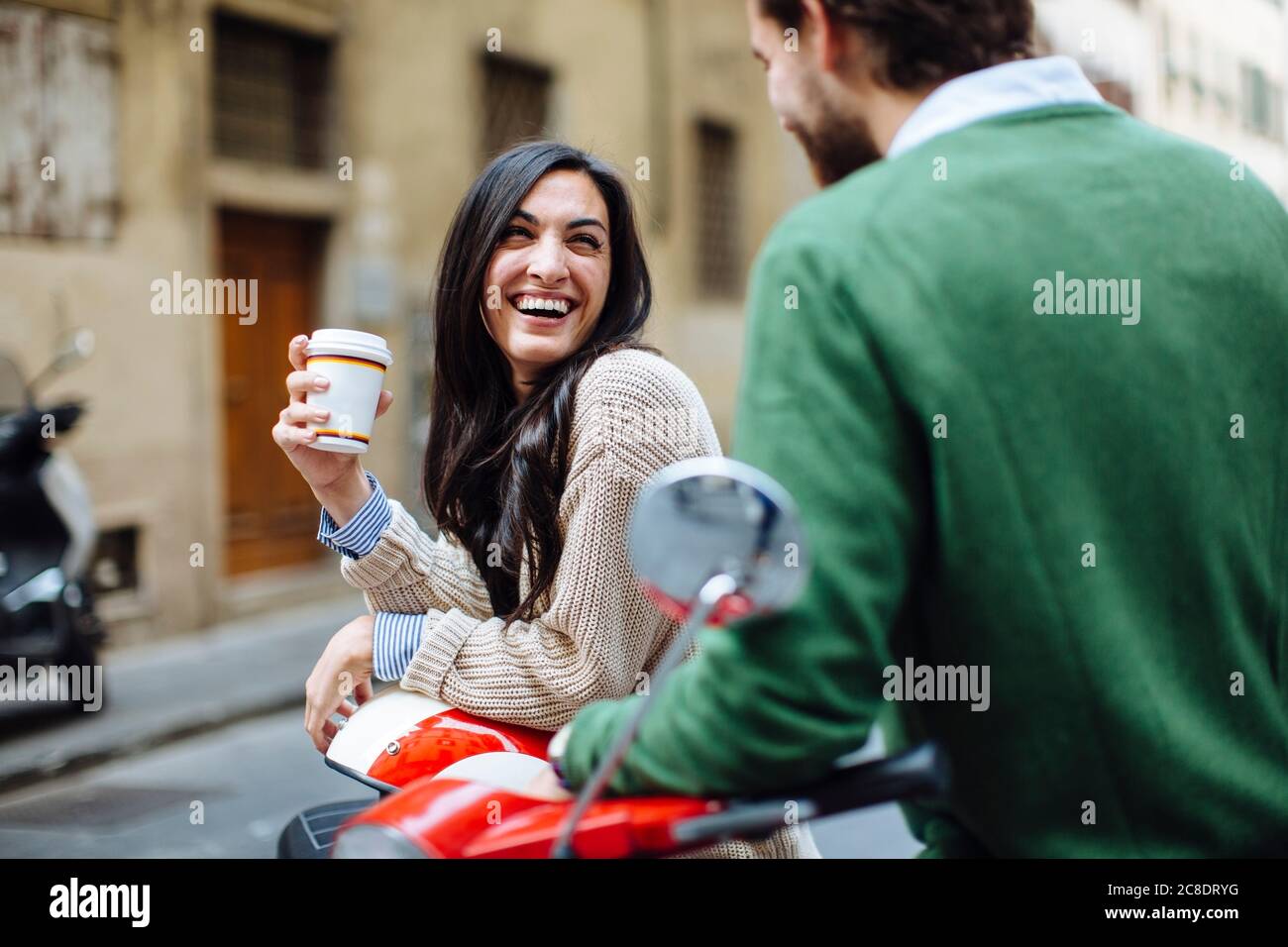 Bonne femme tenant un café en regardant le petit ami tout en s'appuyant sur Vespa Banque D'Images