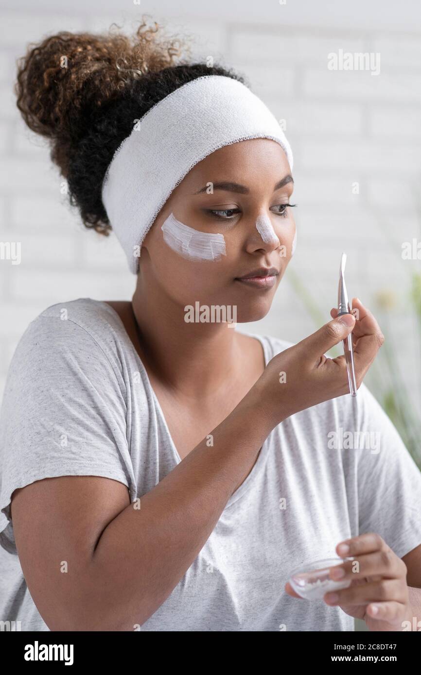 Gros plan d'une jeune femme portant un serre-tête appliquant un masque facial avec brosse à la maison Banque D'Images