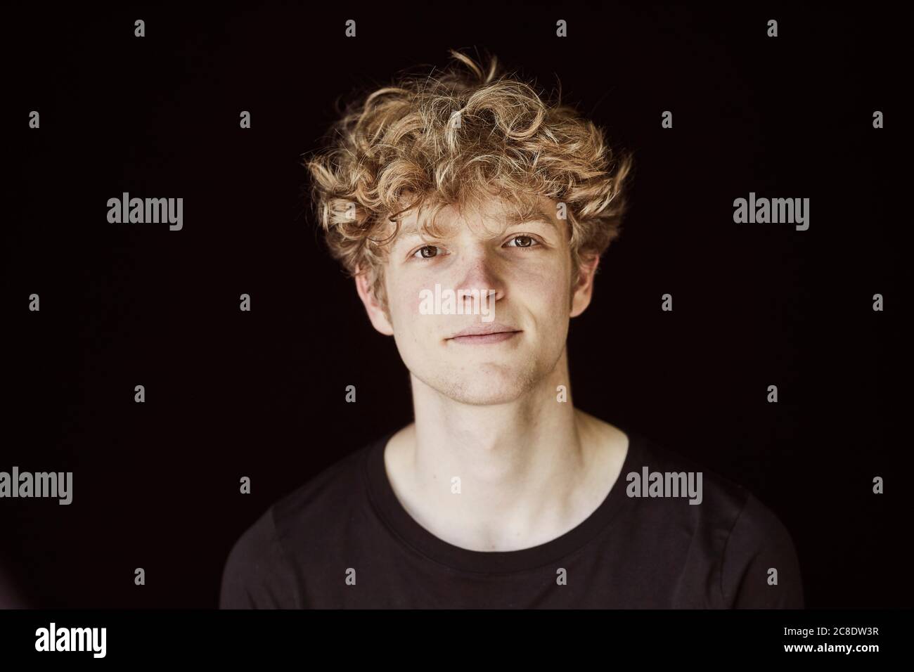 Portrait d'un jeune homme aux cheveux bouclés blonds contre le noir  arrière-plan Photo Stock - Alamy
