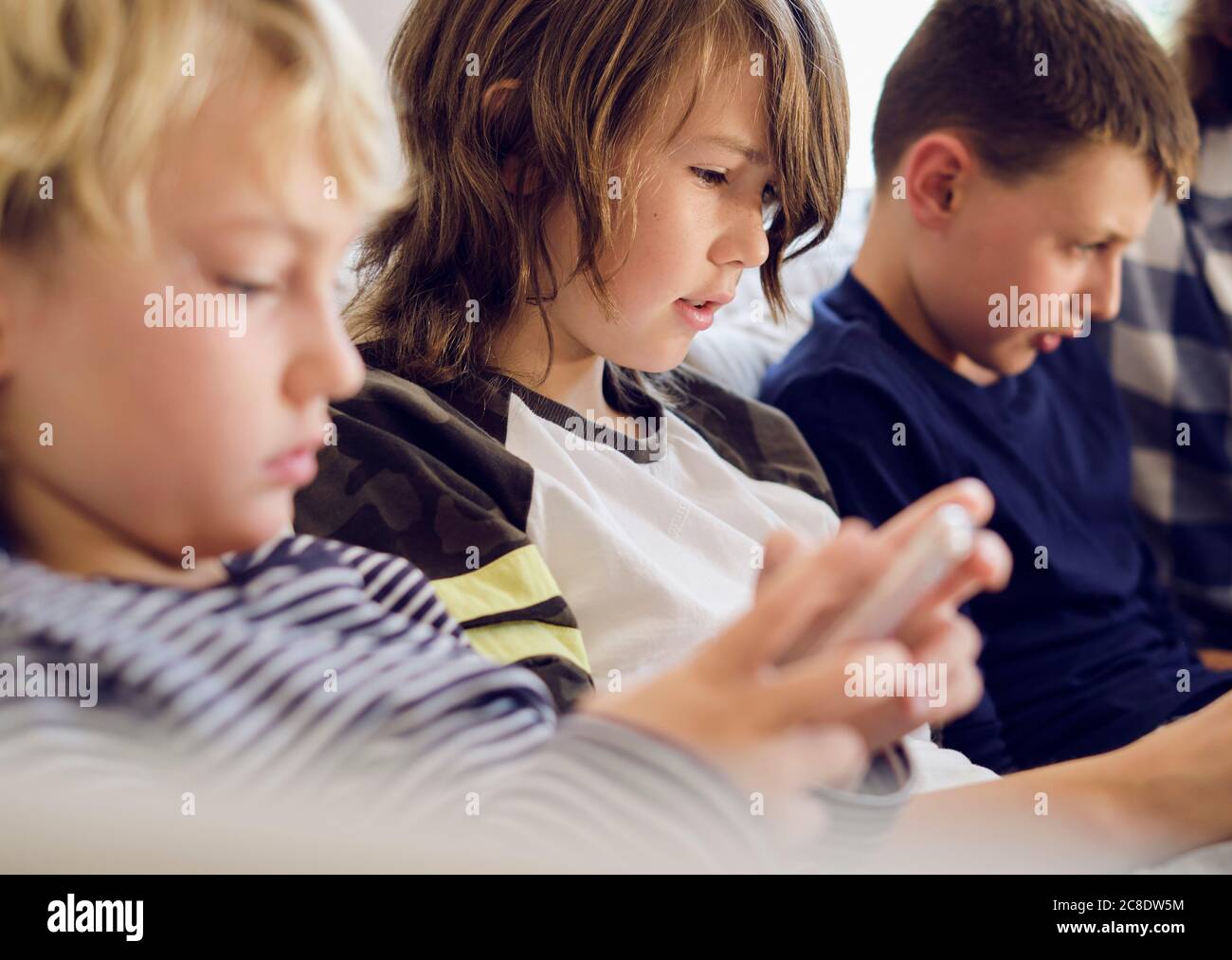 Garçon jouant à des jeux sur smartphone avec la famille en arrière-plan au salon Banque D'Images