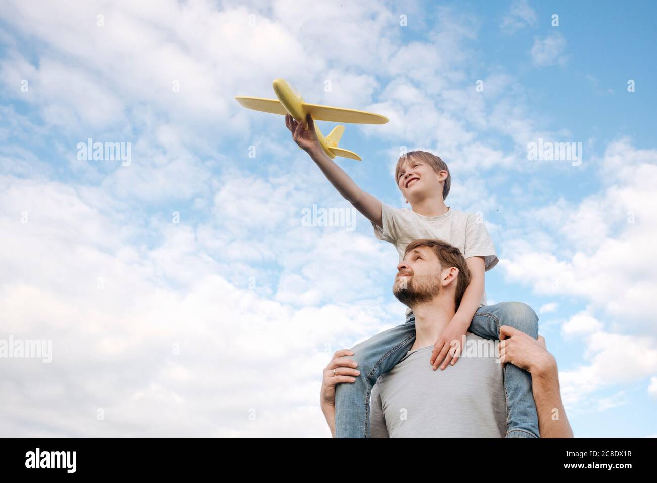 Homme portant son fils sur les épaules jouant avec l'avion jouet contre ciel Banque D'Images