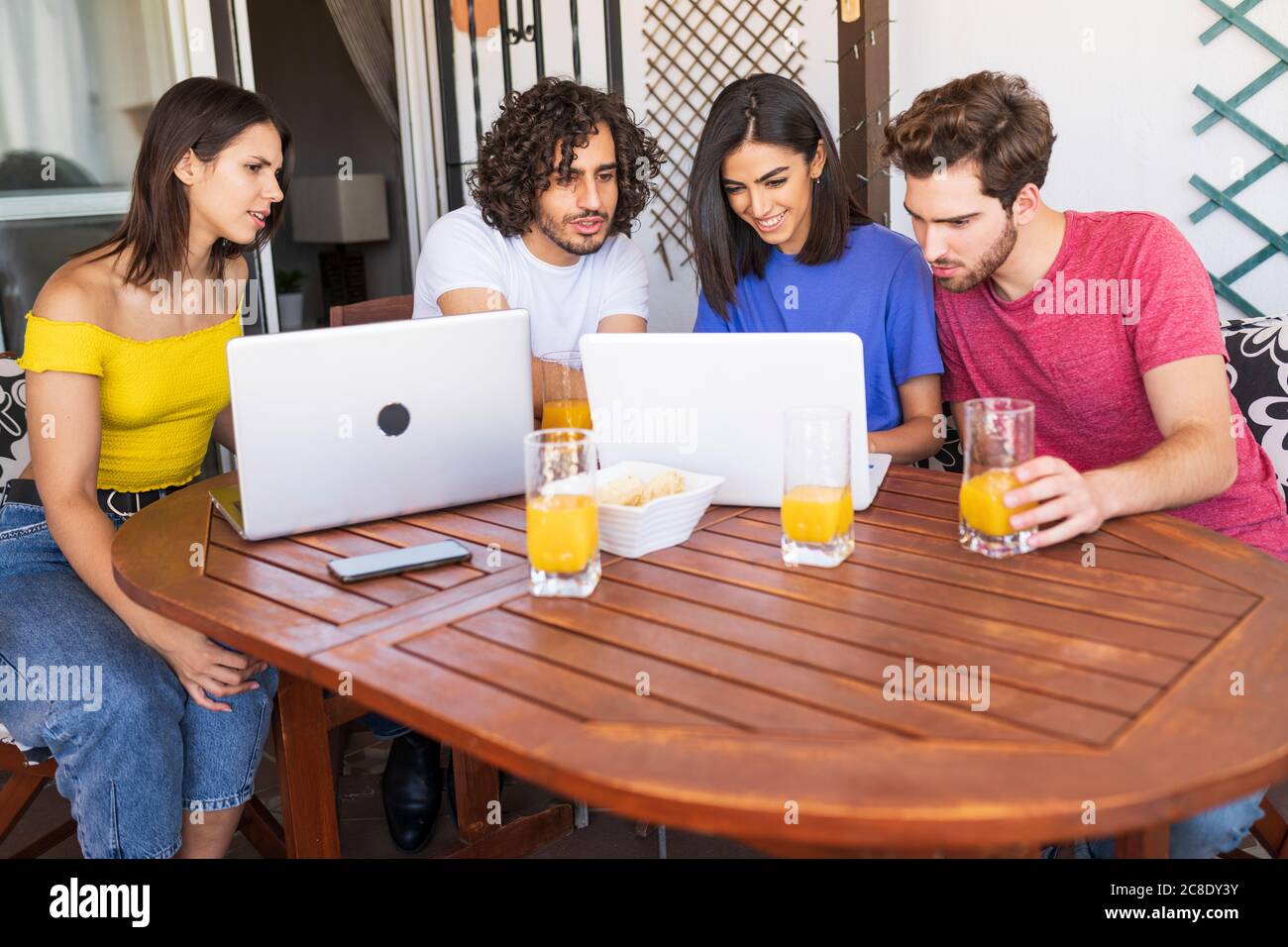 Les jeunes hommes et les jeunes femmes partagent leur ordinateur portable tout en étant assis à une table dans la cour arrière Banque D'Images
