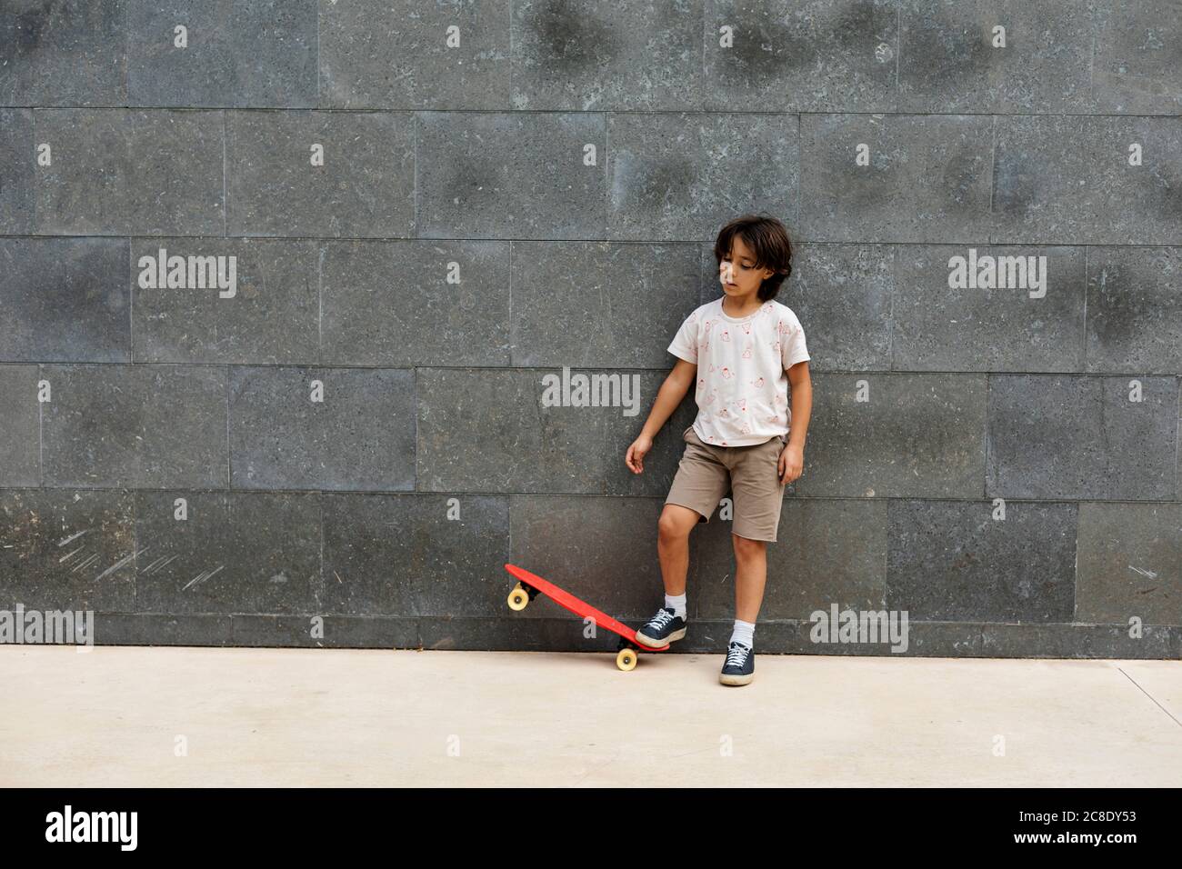 Garçon jouant avec un skateboard tout en restant debout sur le sentier contre le mur Banque D'Images