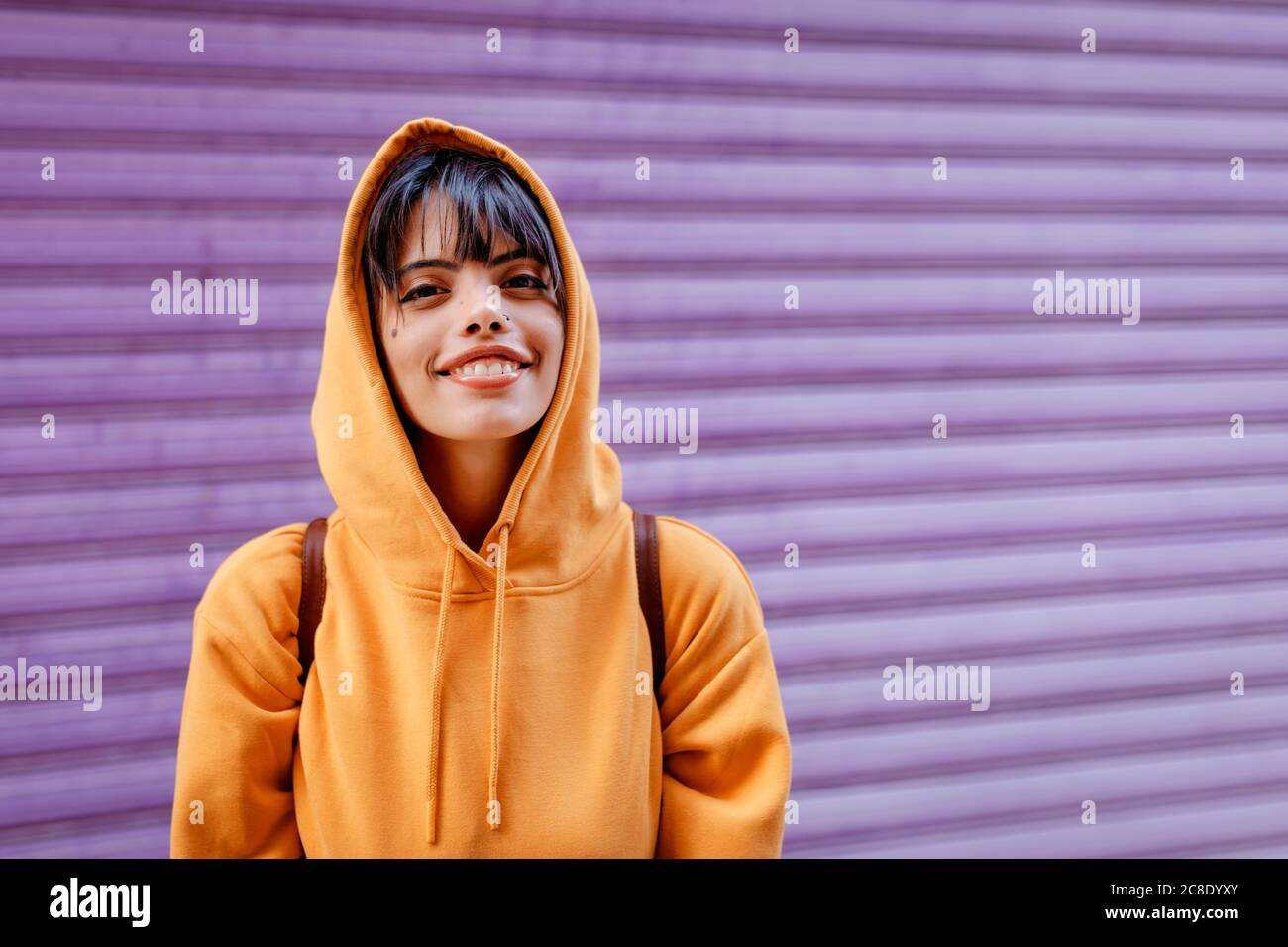 Portrait de la jeune femme avec le sweat à capuche jaune devant arrière-plan violet Banque D'Images