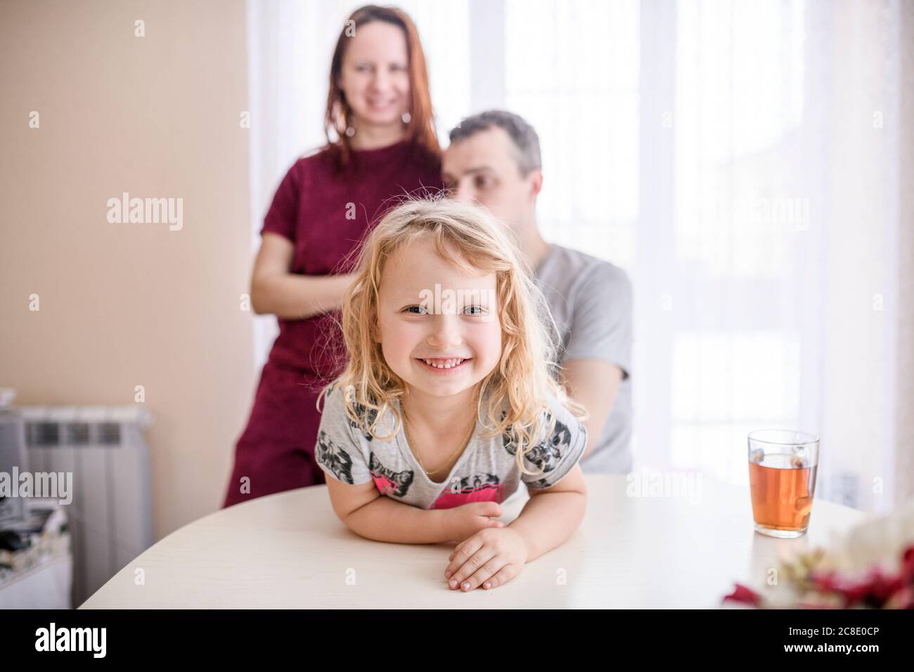 Bonne jolie fille penchée sur la table à manger avec les parents debout en arrière-plan à la maison Banque D'Images