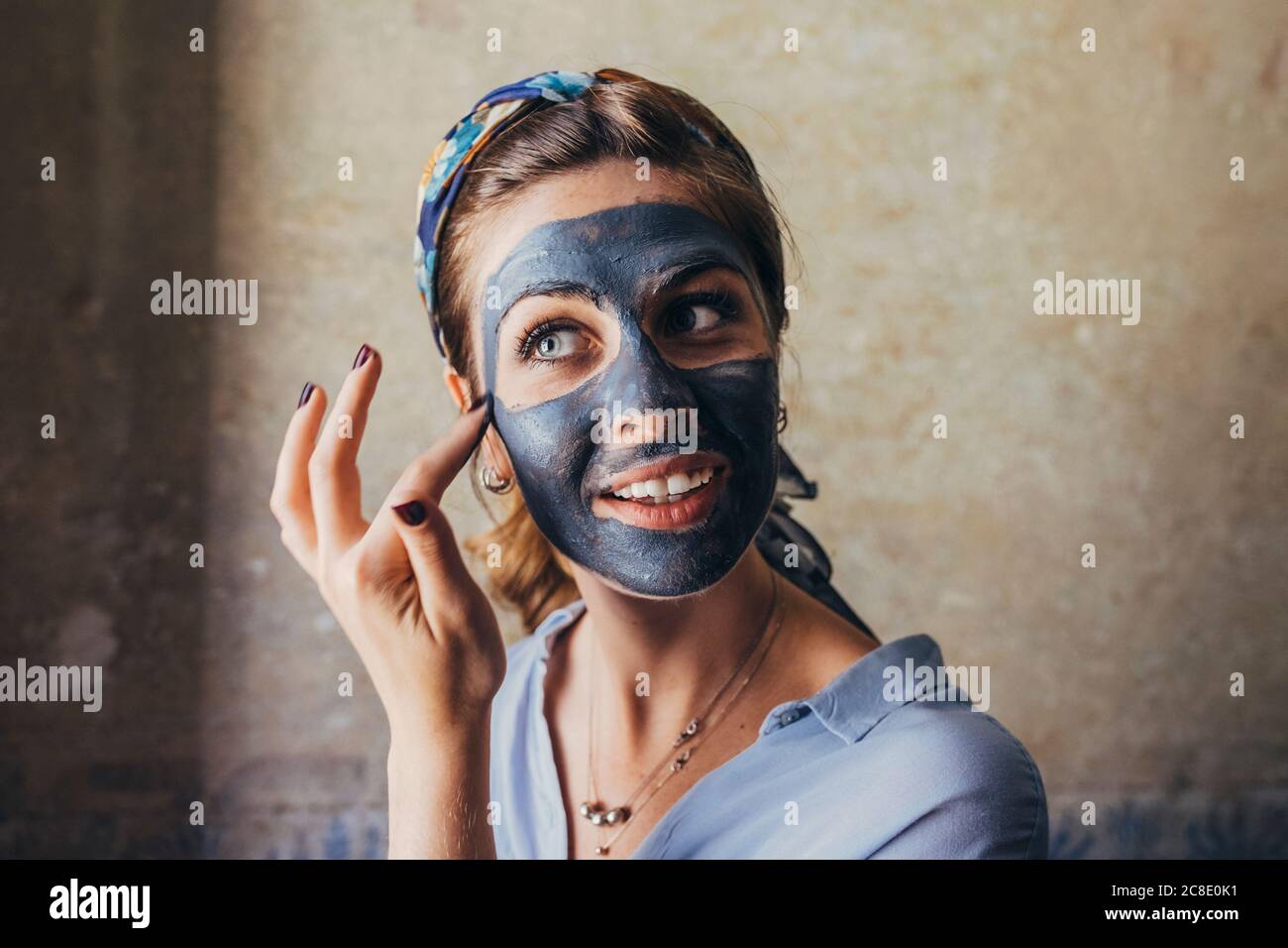 Gros plan de la jeune femme appliquant un masque facial tout en regardant loin à la maison Banque D'Images