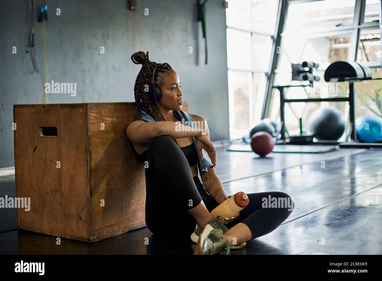 Une athlète féminine attentive écoute de la musique tout en étant assise sur le sol salle de sport Banque D'Images