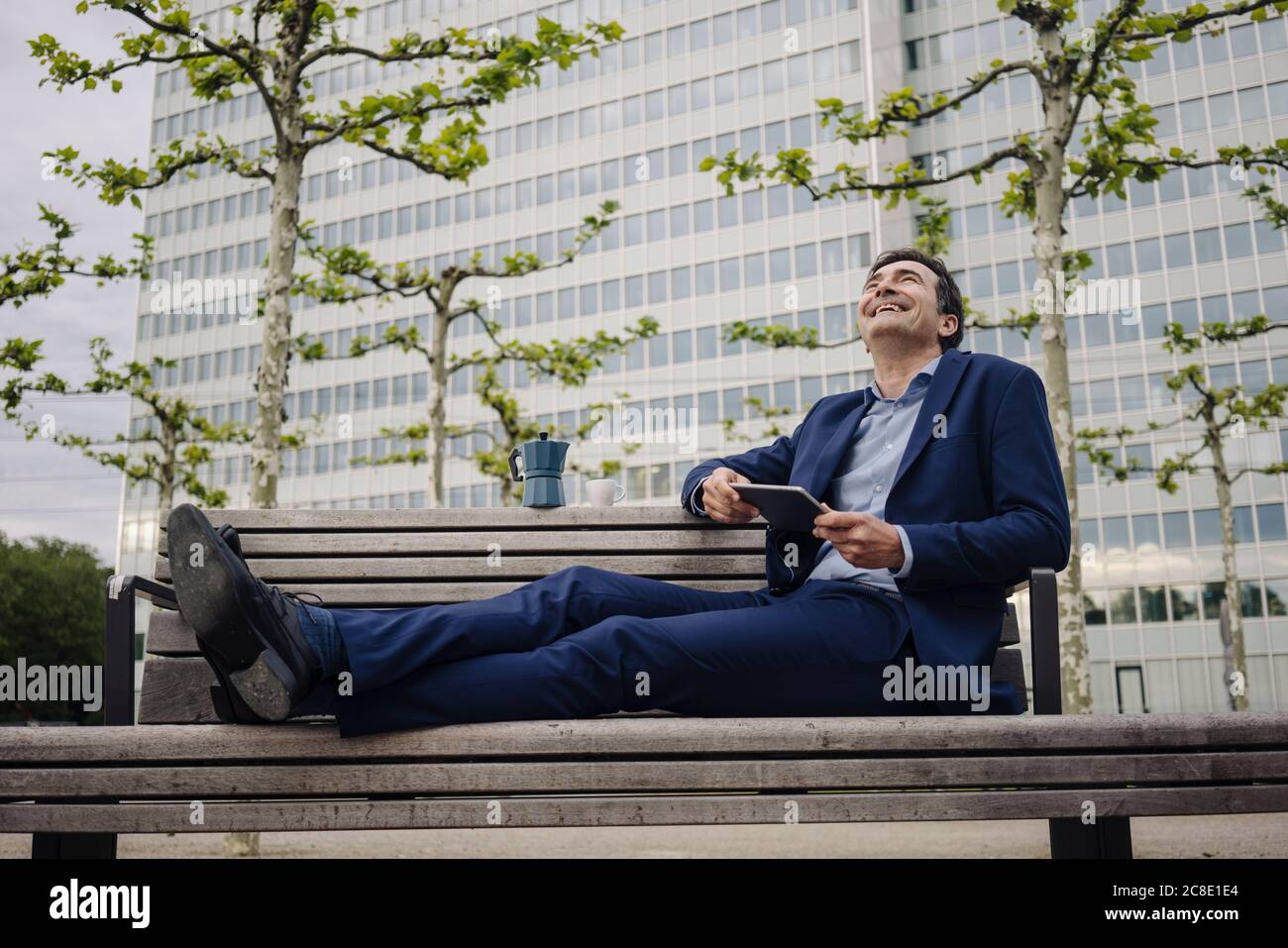 Heureux homme d'affaires mature assis sur un banc dans la ville avec moka pot et tablette Banque D'Images