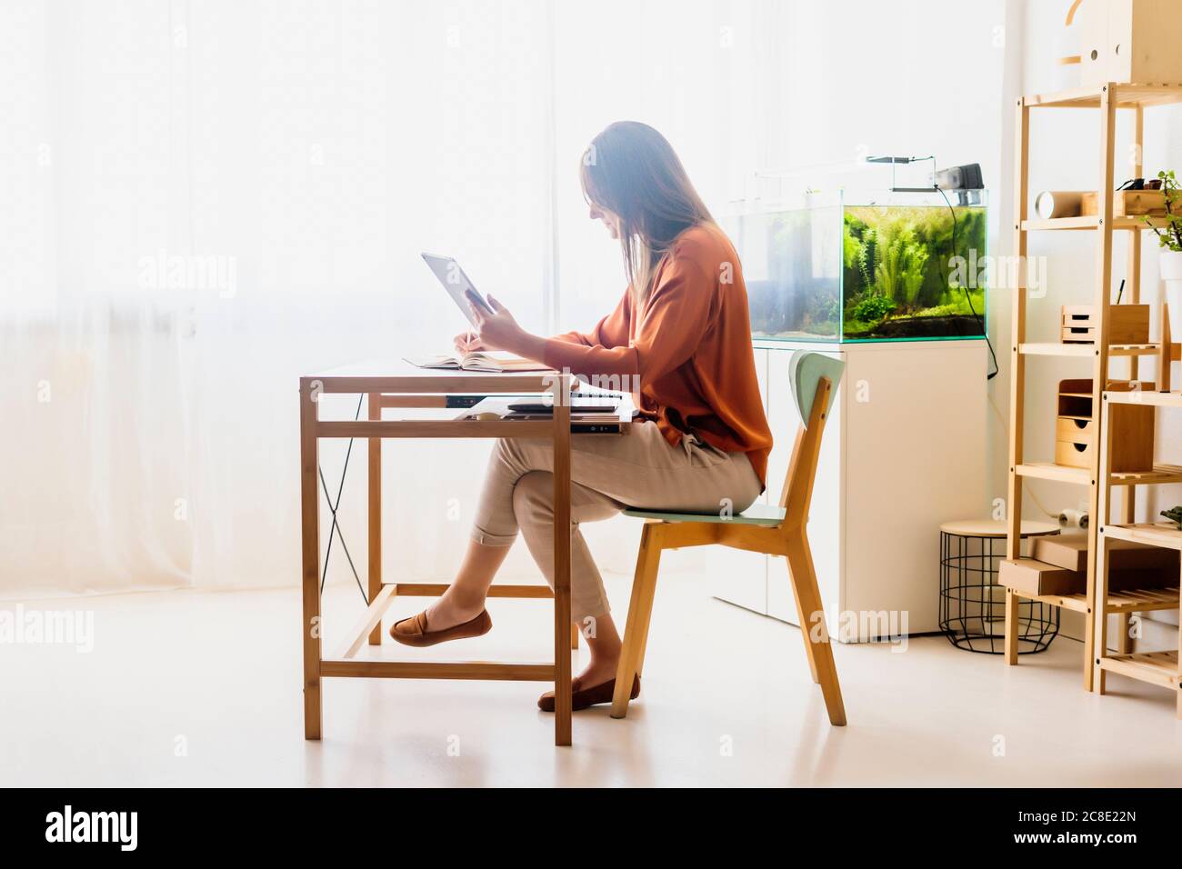 Femme indépendante travaillant à la maison assise au bureau à l'aide d'une tablette Banque D'Images