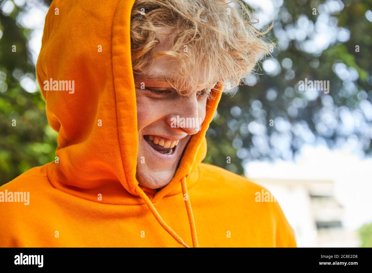 Portrait d'un jeune homme en train de rire portant une chemise à capuche orange Banque D'Images