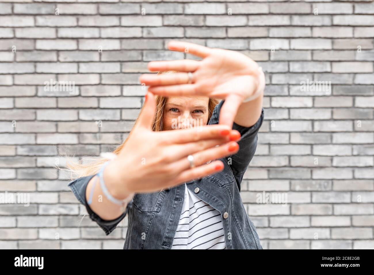 Gros plan de la femme adulte de taille moyenne faisant le cadre du doigt contre le gris mur de briques Banque D'Images