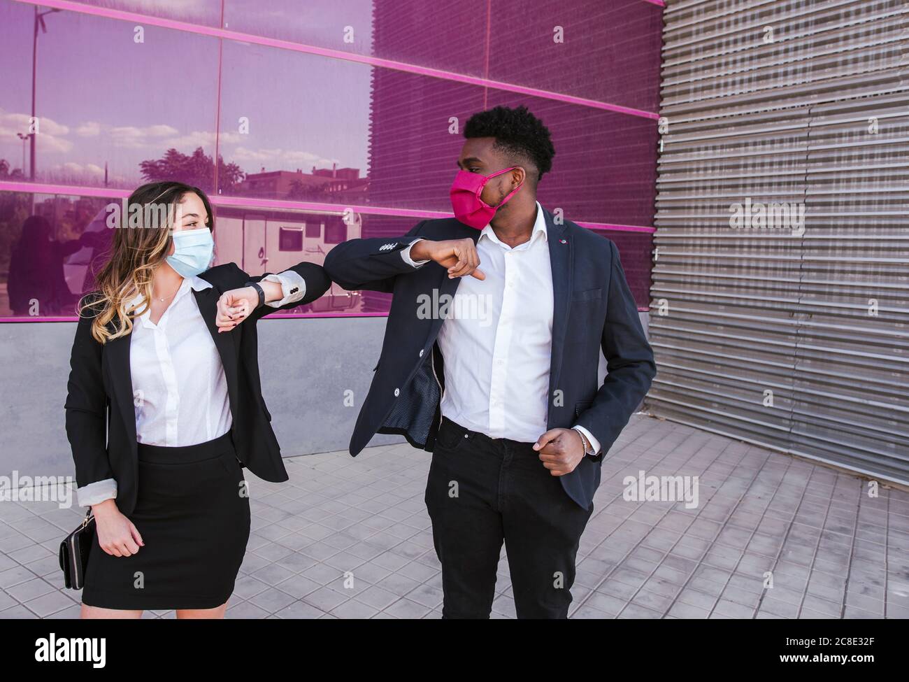 Les gens d'affaires portant des masques donnant une bosse de coude tout en se tenant contre bâtiment moderne Banque D'Images