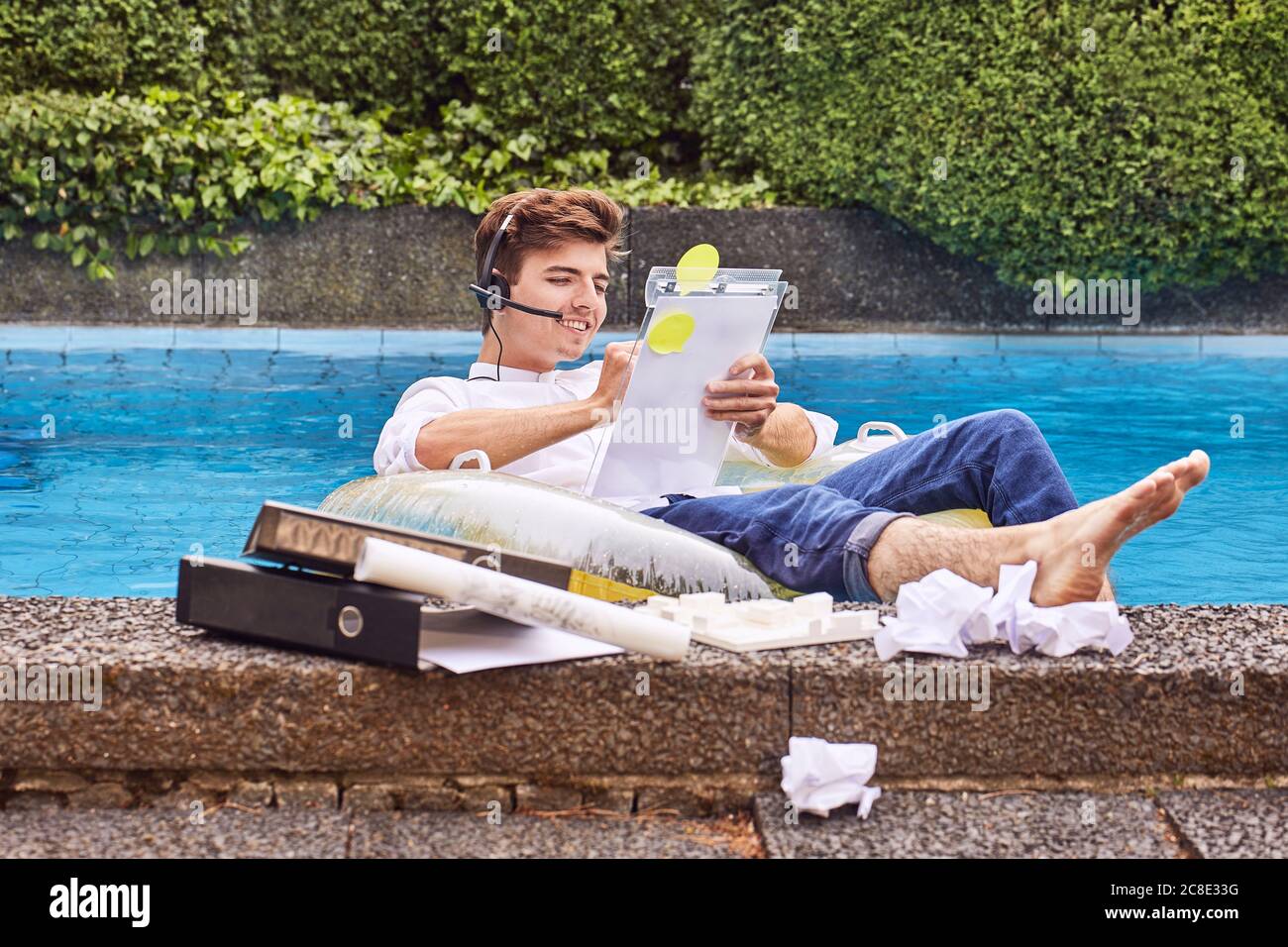 Jeune homme assis sur un matelas pneumatique dans la piscine et travaillant Banque D'Images