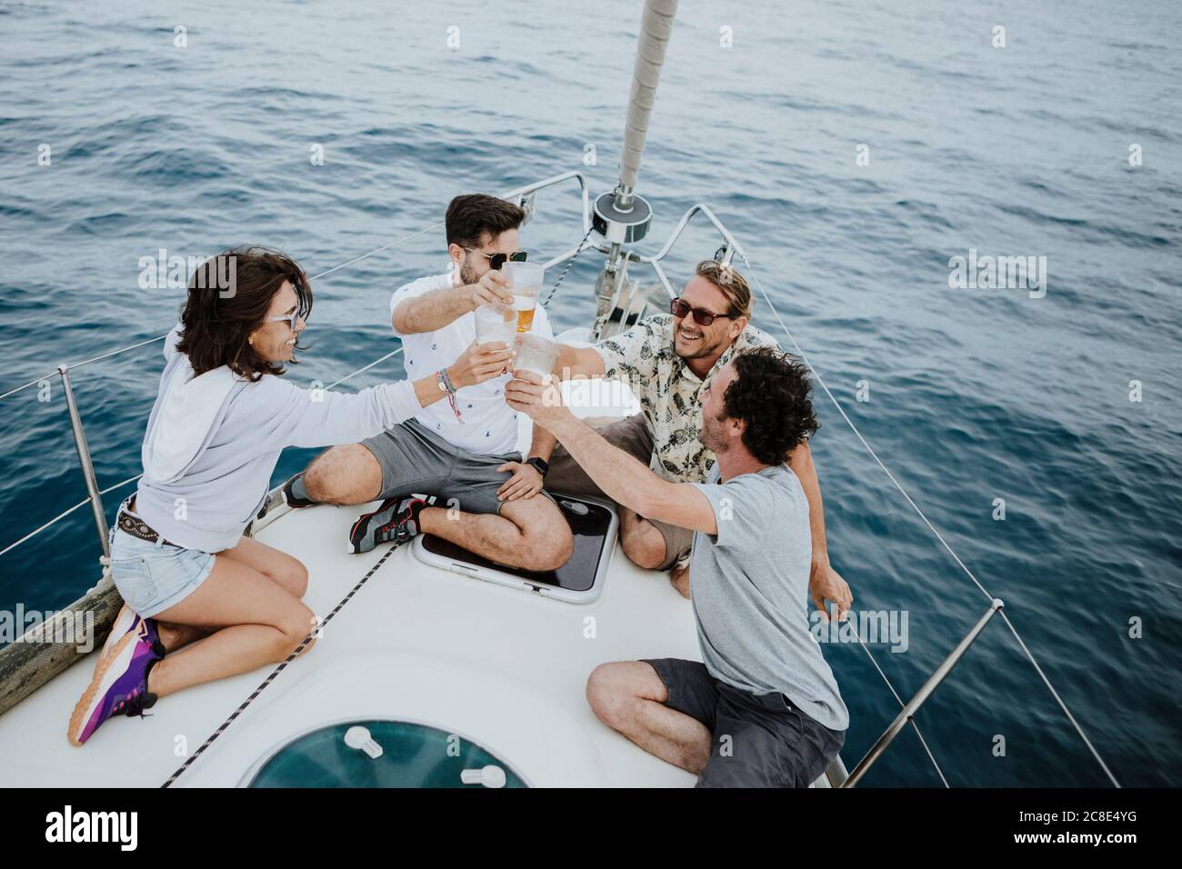 Des amis insouciants qui toastent des verres à bière tout en étant assis sur un voilier à l'intérieur mer Banque D'Images