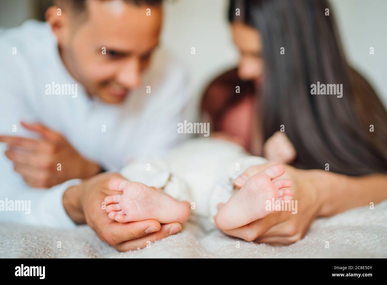 Parents tenant les pieds de bébé garçon sur le lit à la maison Banque D'Images