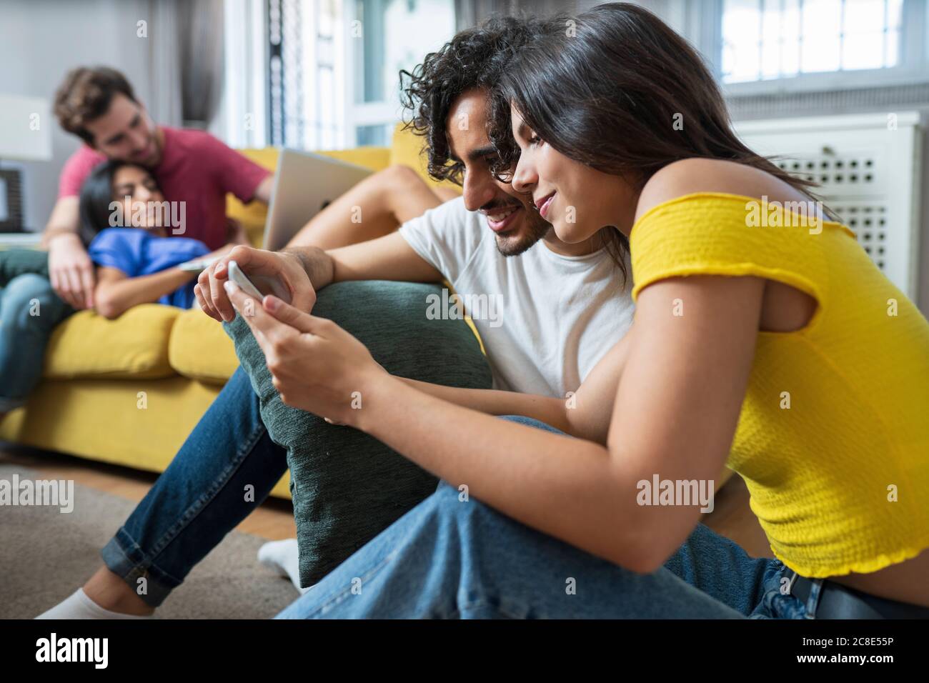 Un jeune couple partage sa table numérique pendant que ses amis se détendent dans la vie chambre à la maison Banque D'Images