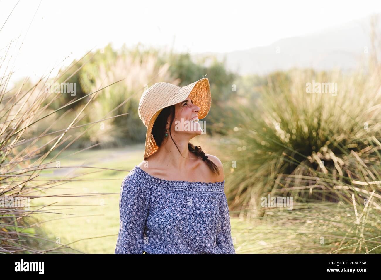 Jeune femme gaie regardant loin en portant un chapeau de soleil à campagne Banque D'Images