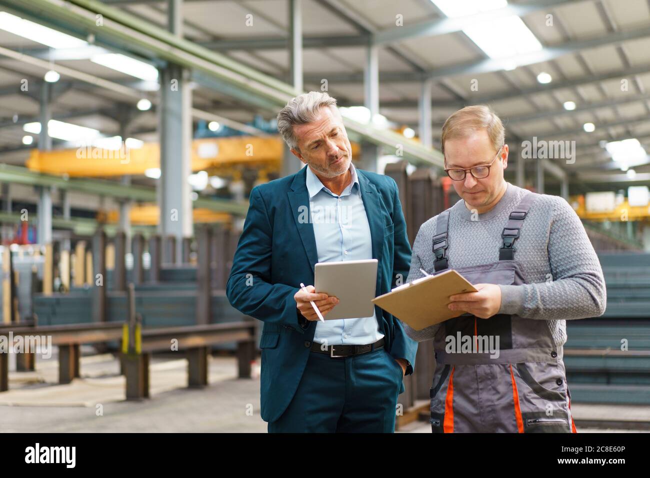 Homme d'affaires avec tablette et employé avec presse-papiers dans une usine Banque D'Images