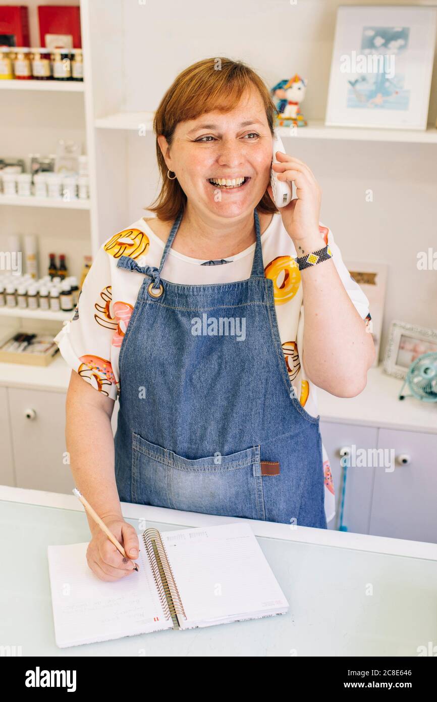 Femme mûre souriante prenant la commande par téléphone dans la boutique de gâteaux Banque D'Images